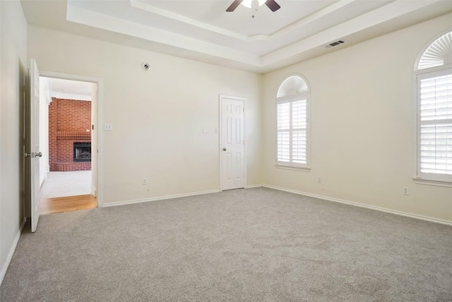 spare room with light carpet, ceiling fan, a tray ceiling, and visible vents