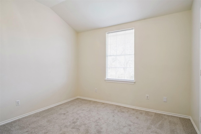 empty room featuring lofted ceiling, light carpet, and baseboards