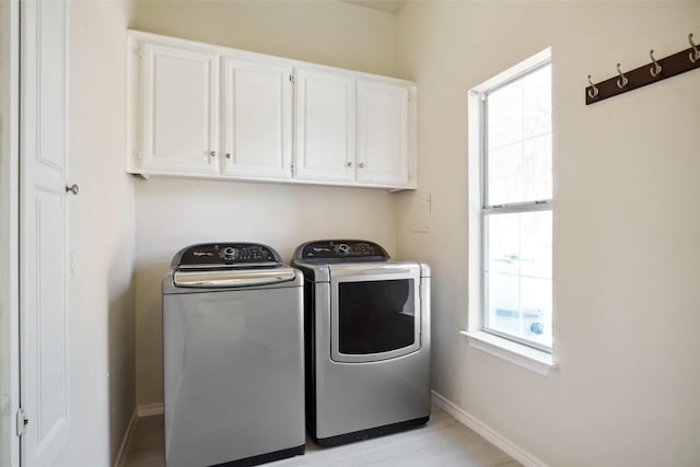 clothes washing area with separate washer and dryer, light wood-style floors, cabinet space, and baseboards