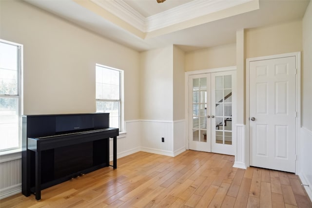 living area featuring french doors, a wainscoted wall, a raised ceiling, and light wood-style flooring