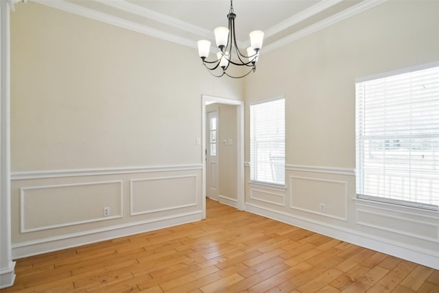 unfurnished dining area with light wood-style flooring, a chandelier, a decorative wall, and crown molding