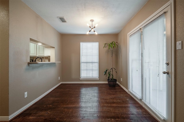 unfurnished dining area with dark hardwood / wood-style flooring, a chandelier, and a textured ceiling