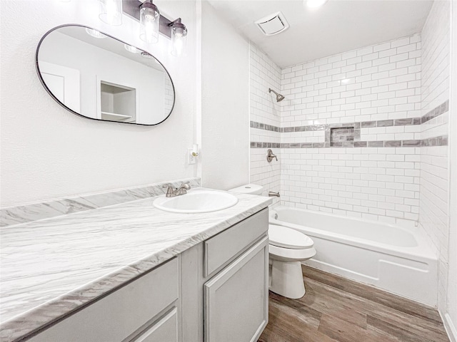 full bathroom featuring tiled shower / bath, vanity, toilet, and hardwood / wood-style floors