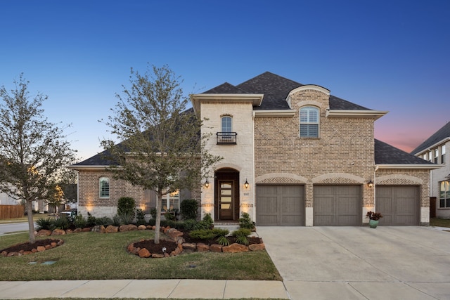 french country style house featuring a garage, brick siding, driveway, roof with shingles, and a lawn