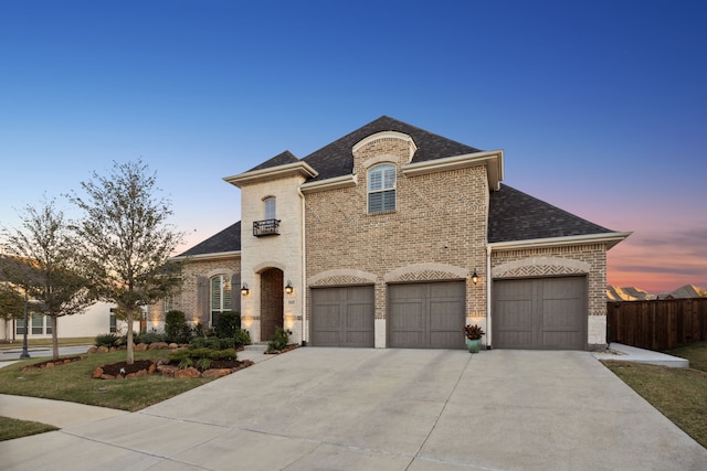 french country style house with a garage, brick siding, fence, concrete driveway, and roof with shingles