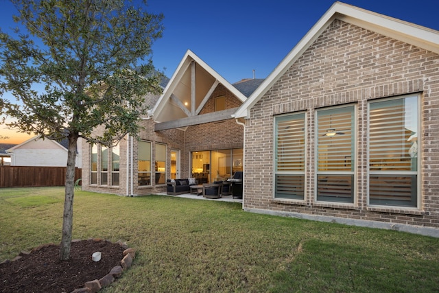 back house at dusk with an outdoor hangout area, a patio, and a lawn