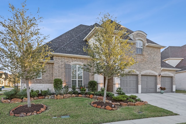 french country home with brick siding, roof with shingles, an attached garage, driveway, and a front lawn