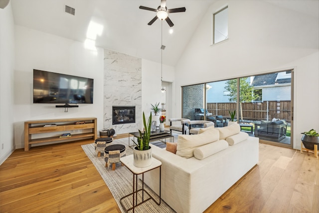 living room with a premium fireplace, high vaulted ceiling, light hardwood / wood-style floors, and ceiling fan