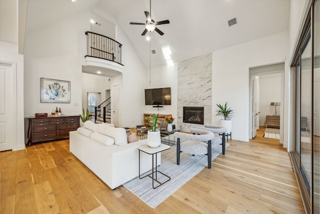 living room with ceiling fan, a fireplace, a high ceiling, and light wood-type flooring