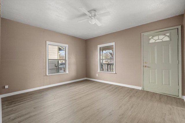 interior space with baseboards, a ceiling fan, wood finished floors, and a healthy amount of sunlight