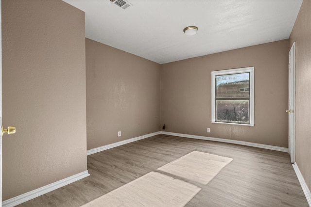 empty room with baseboards, visible vents, and wood finished floors