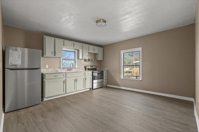 kitchen with sink, light stone counters, a textured ceiling, appliances with stainless steel finishes, and light wood-type flooring