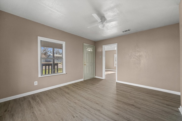 spare room featuring baseboards, ceiling fan, wood finished floors, and visible vents