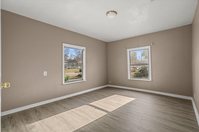 spare room with baseboards, plenty of natural light, and wood finished floors