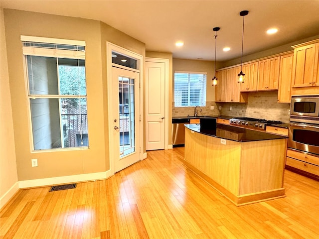 kitchen featuring appliances with stainless steel finishes, pendant lighting, sink, decorative backsplash, and a center island