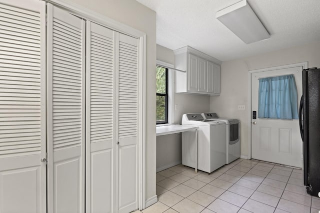 clothes washing area featuring light tile patterned flooring, a textured ceiling, cabinets, and washing machine and clothes dryer