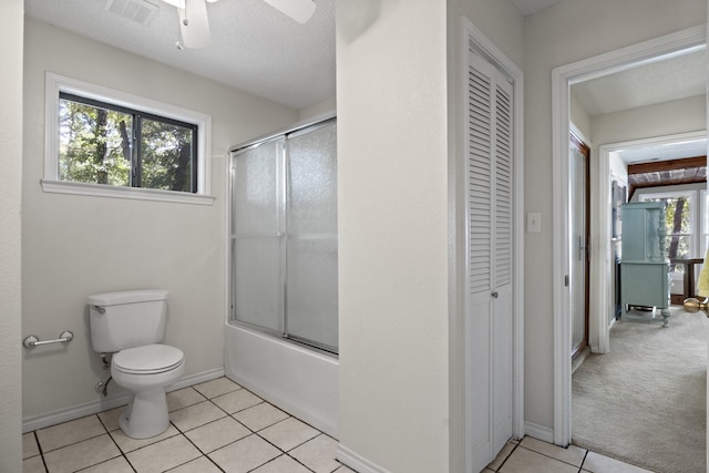 bathroom featuring bath / shower combo with glass door, tile patterned flooring, ceiling fan, toilet, and a textured ceiling