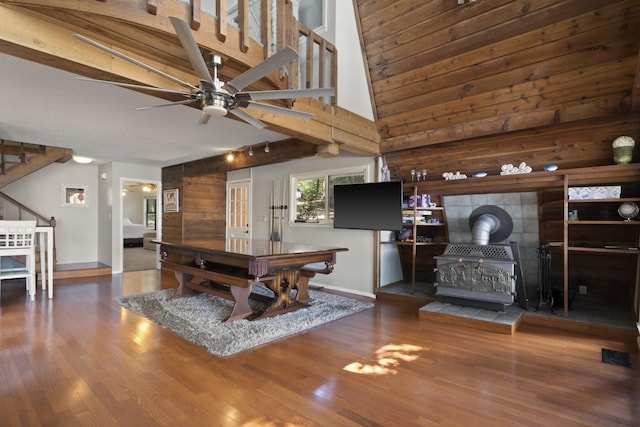 recreation room with dark wood-type flooring, wooden walls, ceiling fan, and a wood stove