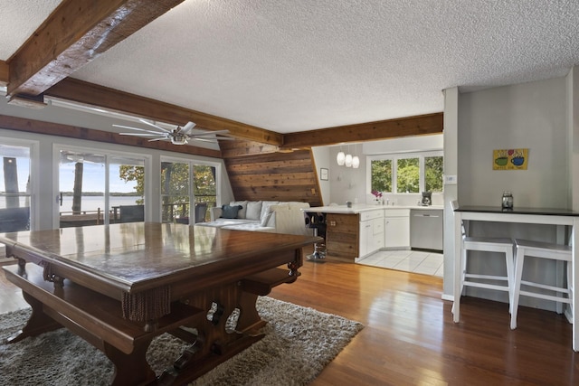 interior space featuring ceiling fan with notable chandelier, a water view, light wood-type flooring, a textured ceiling, and beam ceiling