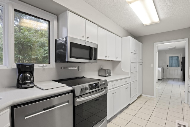 kitchen featuring light tile patterned flooring, a textured ceiling, washer / dryer, white cabinets, and appliances with stainless steel finishes