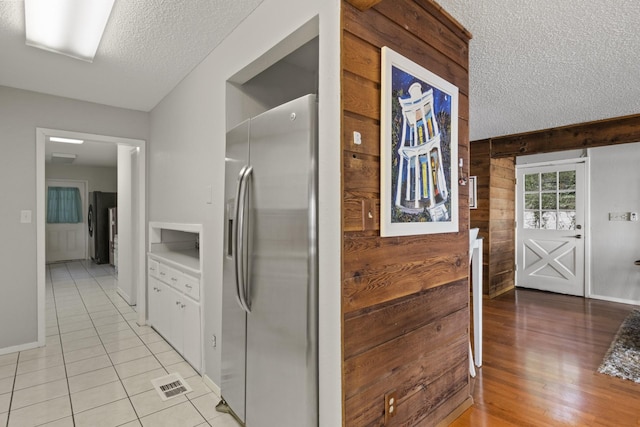 kitchen with wooden walls, stainless steel fridge, light tile patterned floors, a textured ceiling, and stainless steel fridge with ice dispenser