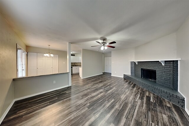 unfurnished living room with dark hardwood / wood-style flooring, a fireplace, and ceiling fan with notable chandelier