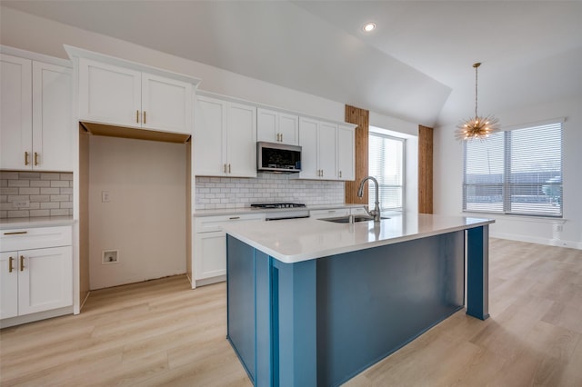 kitchen featuring decorative light fixtures, white cabinetry, sink, and an island with sink