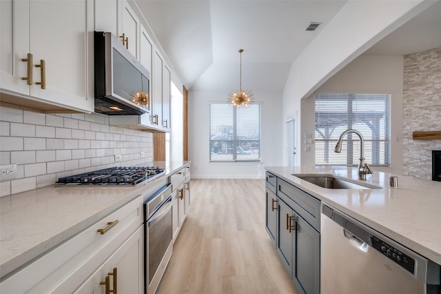 kitchen featuring white cabinets, sink, vaulted ceiling, appliances with stainless steel finishes, and decorative light fixtures