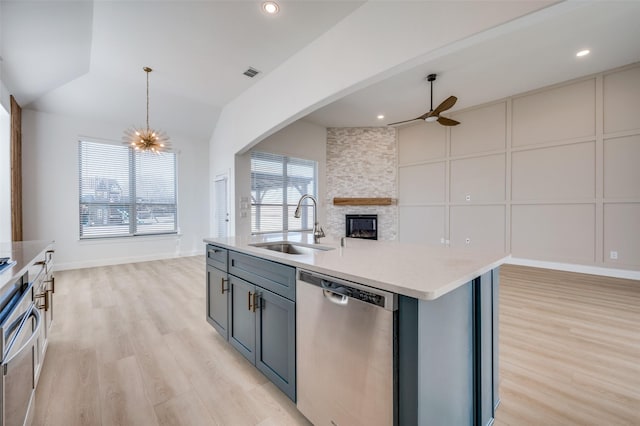 kitchen with a center island with sink, ceiling fan with notable chandelier, sink, stainless steel dishwasher, and light hardwood / wood-style floors