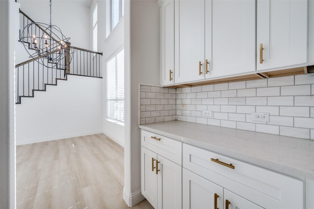 kitchen featuring backsplash, white cabinets, light hardwood / wood-style flooring, light stone countertops, and decorative light fixtures