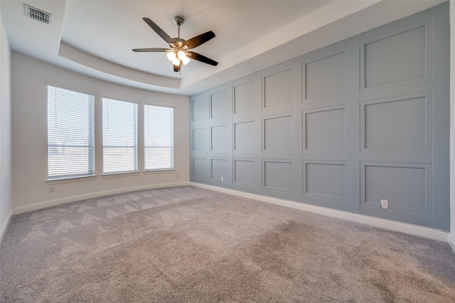 empty room featuring ceiling fan, light colored carpet, and a tray ceiling