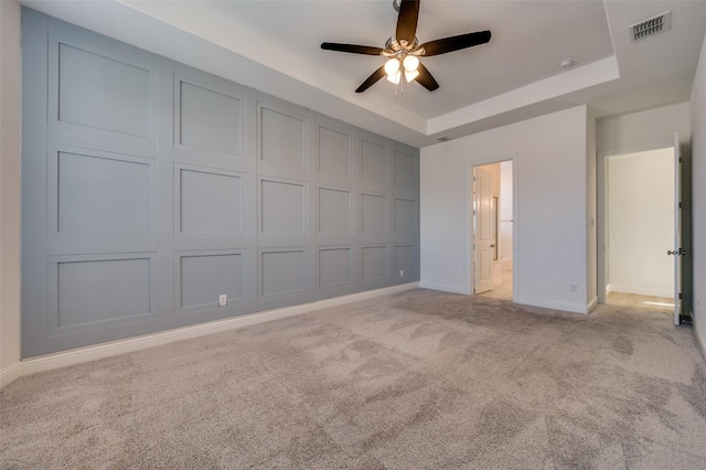 unfurnished bedroom featuring light carpet, ensuite bathroom, ceiling fan, a tray ceiling, and a closet