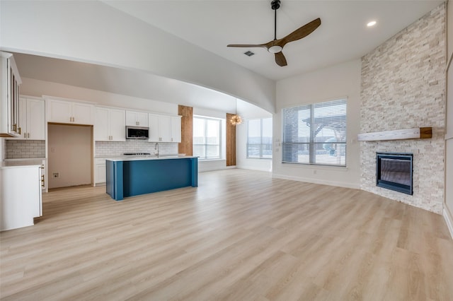 kitchen with tasteful backsplash, a fireplace, ceiling fan with notable chandelier, a kitchen island with sink, and white cabinets