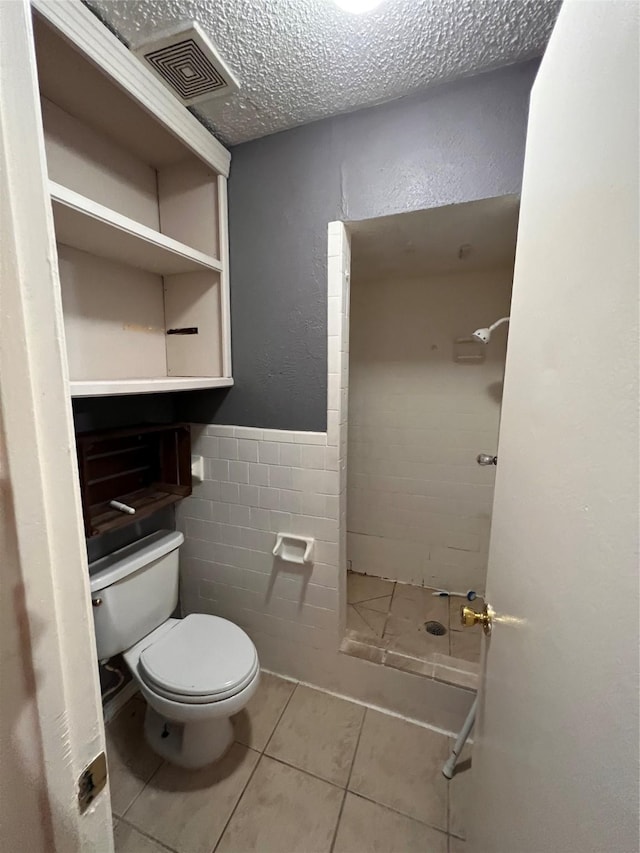 bathroom with tile patterned floors, toilet, a textured ceiling, tile walls, and walk in shower