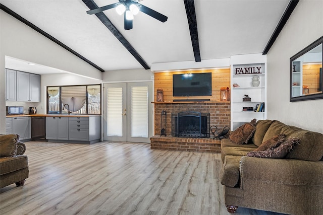 living room with ceiling fan, sink, light hardwood / wood-style flooring, a fireplace, and vaulted ceiling with beams