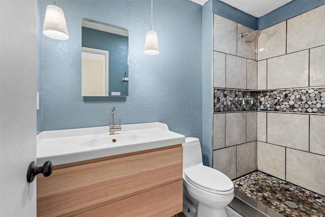 bathroom with a tile shower, vanity, and toilet