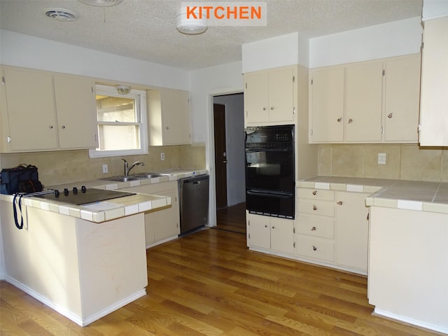 kitchen with sink, tasteful backsplash, tile countertops, light hardwood / wood-style flooring, and black appliances