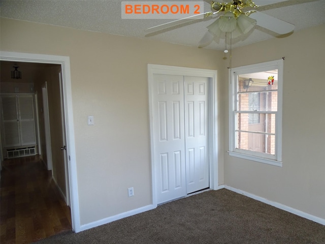 unfurnished bedroom featuring ceiling fan, a textured ceiling, dark carpet, and a closet