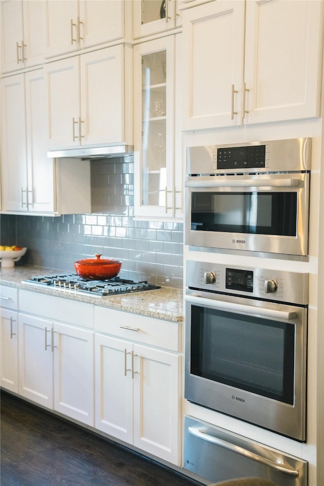 kitchen featuring decorative backsplash, light stone counters, white cabinetry, and appliances with stainless steel finishes