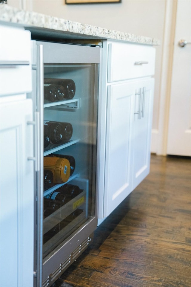 room details with light stone counters, white cabinetry, beverage cooler, and dark hardwood / wood-style floors