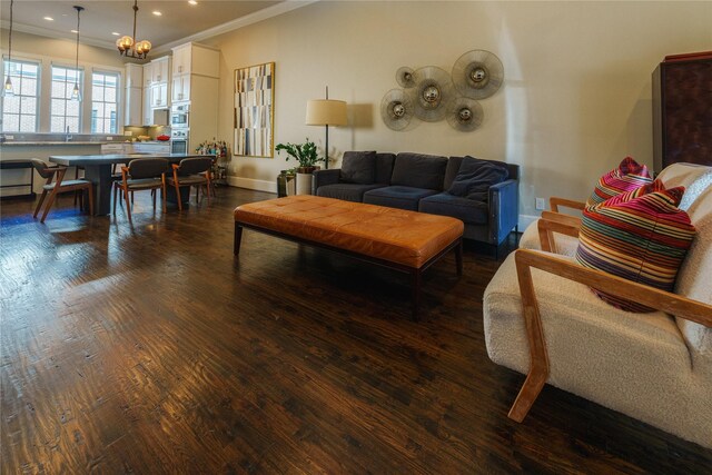 living room with crown molding, sink, dark hardwood / wood-style floors, and an inviting chandelier