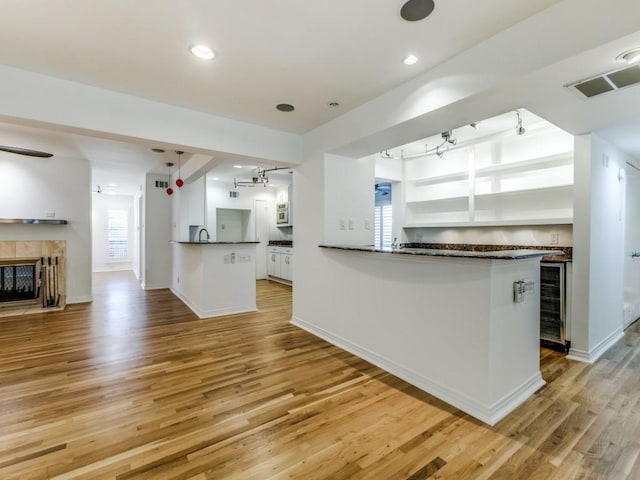 kitchen with a tile fireplace, kitchen peninsula, light hardwood / wood-style flooring, plenty of natural light, and white cabinetry