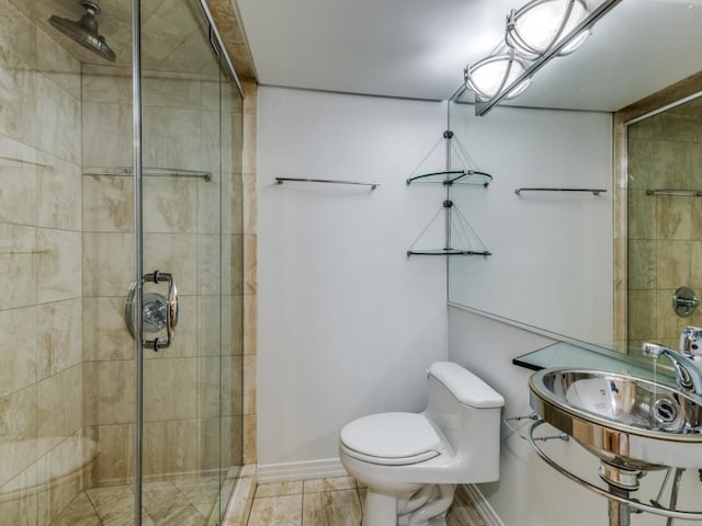 bathroom featuring toilet, a shower with shower door, and sink