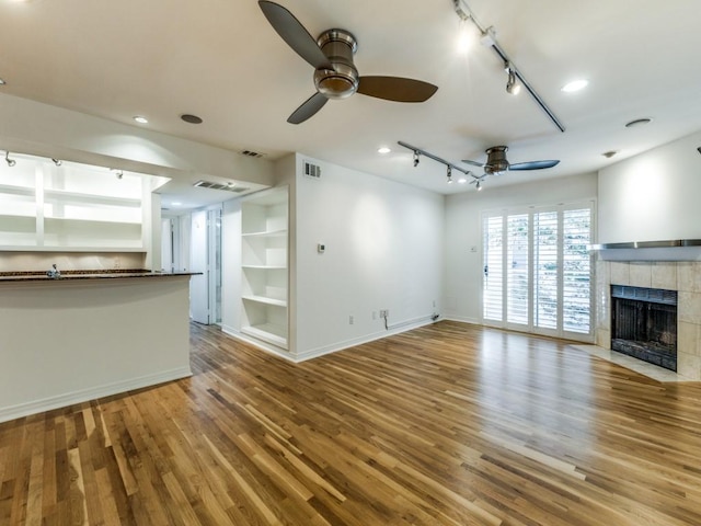 unfurnished living room featuring built in shelves, ceiling fan, light wood-type flooring, and a tiled fireplace