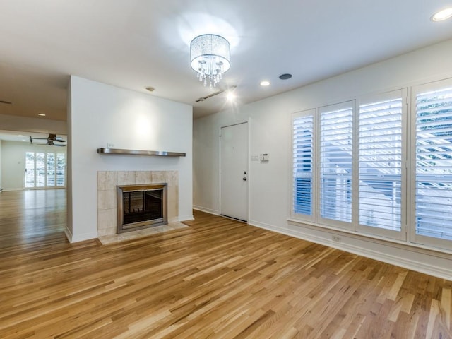 unfurnished living room with a fireplace, ceiling fan with notable chandelier, and light hardwood / wood-style flooring