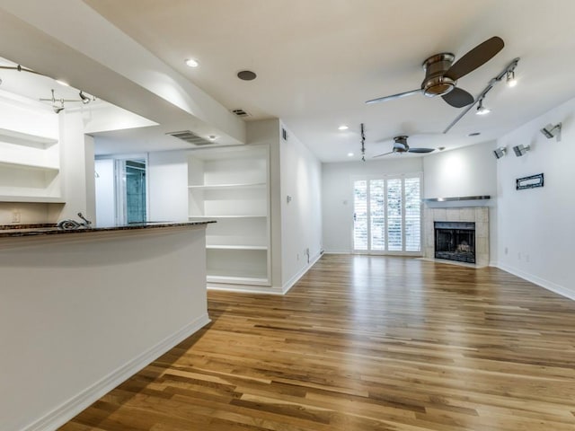 unfurnished living room with built in features, light hardwood / wood-style flooring, ceiling fan, and a tiled fireplace