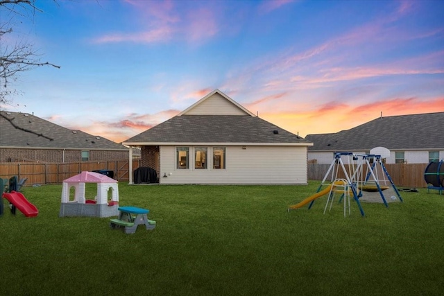 back house at dusk with a lawn and a playground