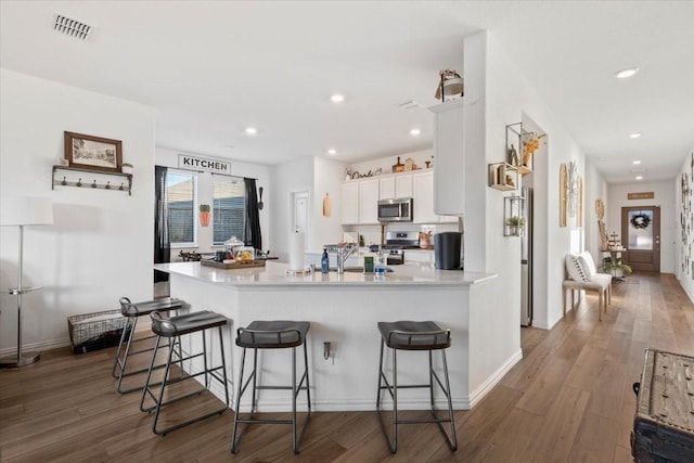 kitchen with white cabinets, a kitchen bar, wood-type flooring, stainless steel appliances, and kitchen peninsula