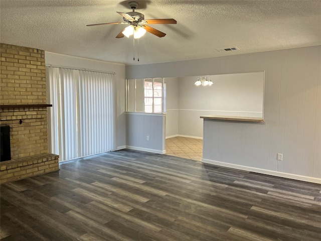 unfurnished living room with a fireplace, ceiling fan with notable chandelier, dark hardwood / wood-style floors, and a textured ceiling