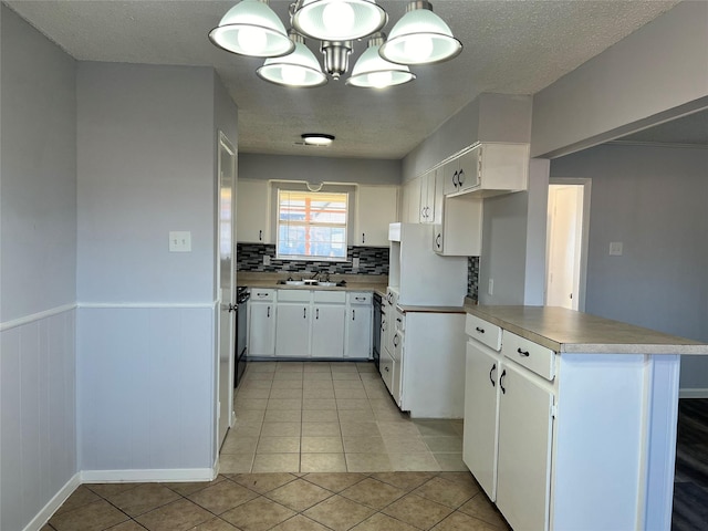 kitchen with light tile patterned flooring, white cabinetry, hanging light fixtures, kitchen peninsula, and backsplash